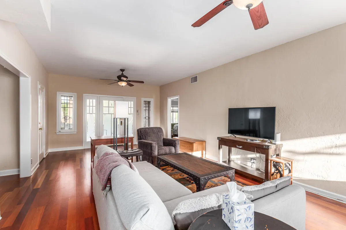 This image captures a cozy living room scene with a plush sofa, an armchair, a coffee table, and a TV, all arranged to encourage relaxation and conversation. Large windows allow natural light to flood the space, highlighting the inviting textures and creating a cheerful, welcoming ambiance perfect for unwinding or socializing.