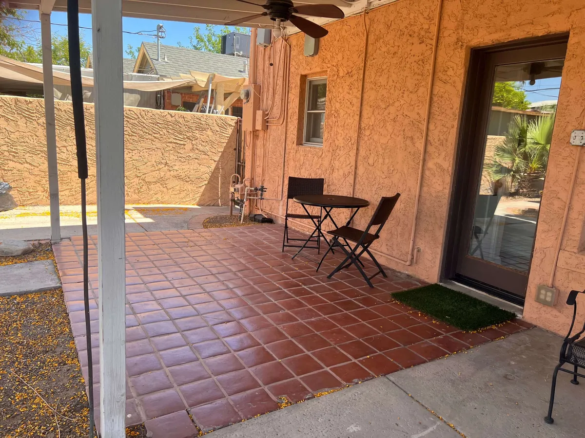This photo showcases an inviting outdoor table and chairs set against a textured wall, with paved flooring and a nearby doorway that hints at easy indoor-outdoor flow. The soft lighting suggests a calm, cozy atmosphere for enjoying a morning coffee or relaxing after a day of exploring.
