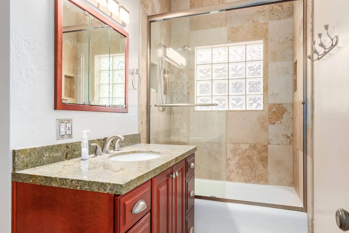 A sparkling clean bathroom featuring a granite countertop vanity with striking red cabinetry and a glass-enclosed shower. The space is modern, well-equipped, and inviting, offering ample room for personal care routines.
