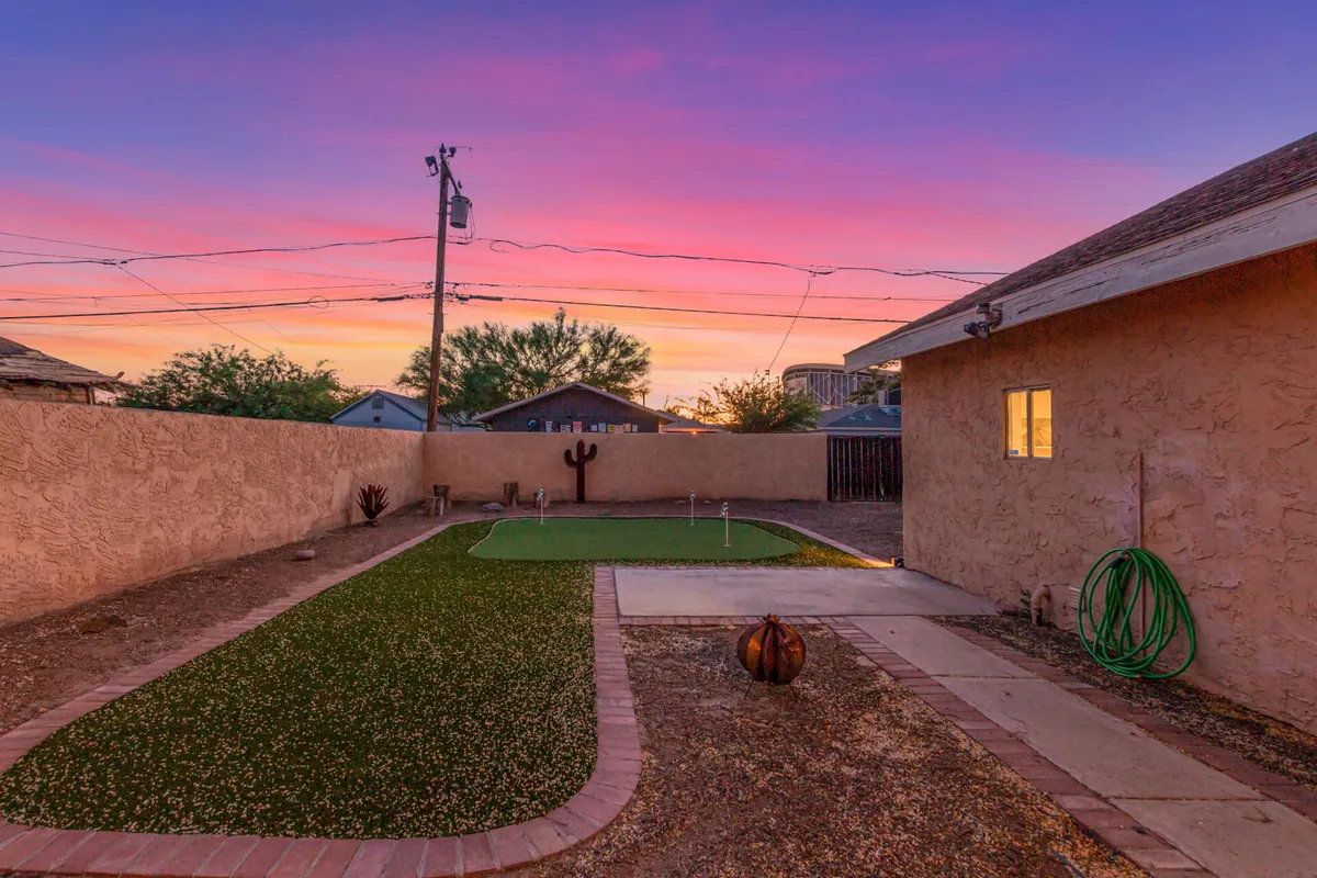 A serene exterior scene featuring a green lawn, a cactus sculpture, and a decorative pumpkin, all beneath a stunning sunset sky. The atmosphere is calm, ideal for relaxation after a busy day.