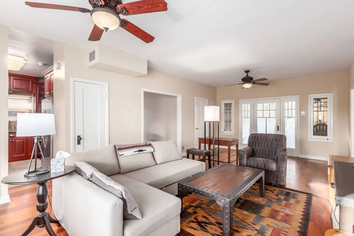 The image portrays a welcoming living room with a plush sofa, coffee table, wooden flooring, lamp, and ceiling fan. The atmosphere is warm and inviting, illuminated by ambient lighting, creating the perfect setting for relaxed evenings.
