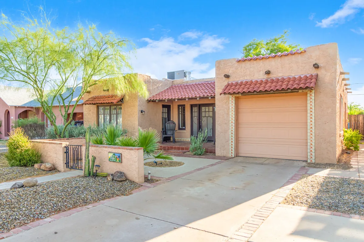 The image focuses on a serene front porch with desert landscaping and decorative wall tiles, creating a peaceful atmosphere for relaxing or greeting the day. The garage and the tidy front yard further emphasize the security and privacy of a single-family home.