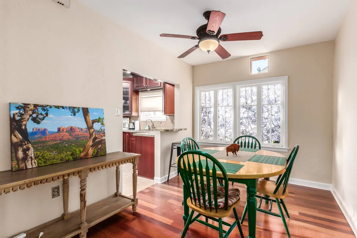 A bright and inviting dining area featuring a wooden dining table with green chairs, a landscape painting on the wall, and a view towards the kitchen. The setting is ideal for family meals, morning coffee, and casual gatherings, radiating a sense of warmth and togetherness.
