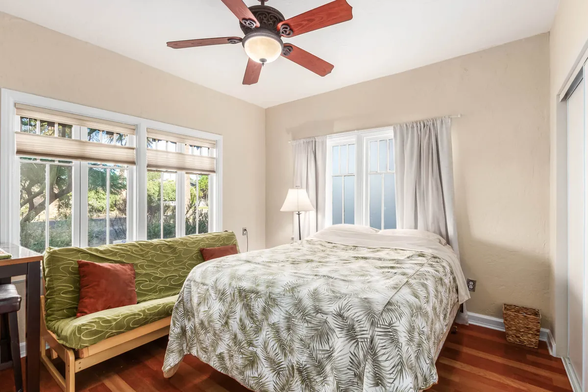 A bright, airy bedroom featuring a bed with plush floral bedding, a cozy green sofa, and large windows allowing abundant natural light to fill the space. The room exudes a tranquil and comfortable ambiance, perfect for unwinding after a day in the city.