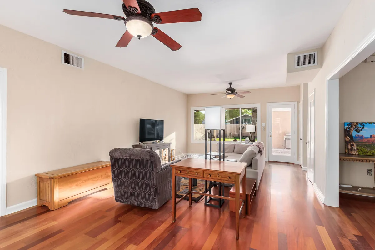 A comfortable living area is shown with a sofa, coffee table, television, and a large window letting in sunlight. The space is arranged for both relaxation and entertaining, ideal for movie nights or friendly get-togethers.