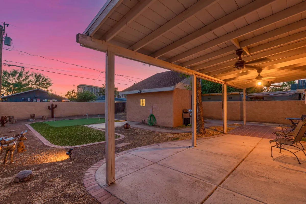 Showcasing a covered patio overlooking a green lawn with decorative sculptures and a warm sunset sky, this image presents a tranquil outdoor space. The lawn offers ample room for both relaxation and pet play, while the patio hints at comfortable, extended outdoor living.