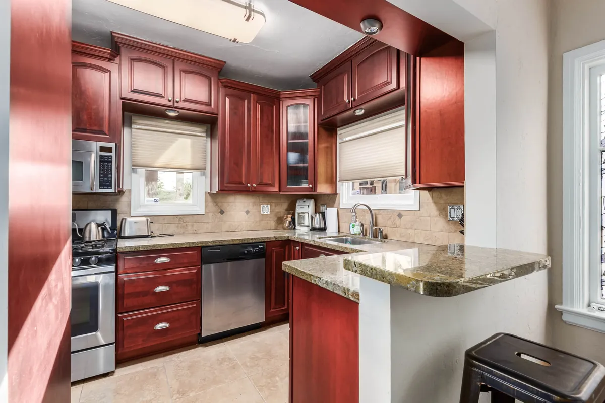 A cozy kitchen with striking red cabinetry, granite countertops, and stainless steel appliances. The space is open and functional, clearly set up for cooking, entertaining, and gathering, with enough room to prepare meals and host small gatherings.