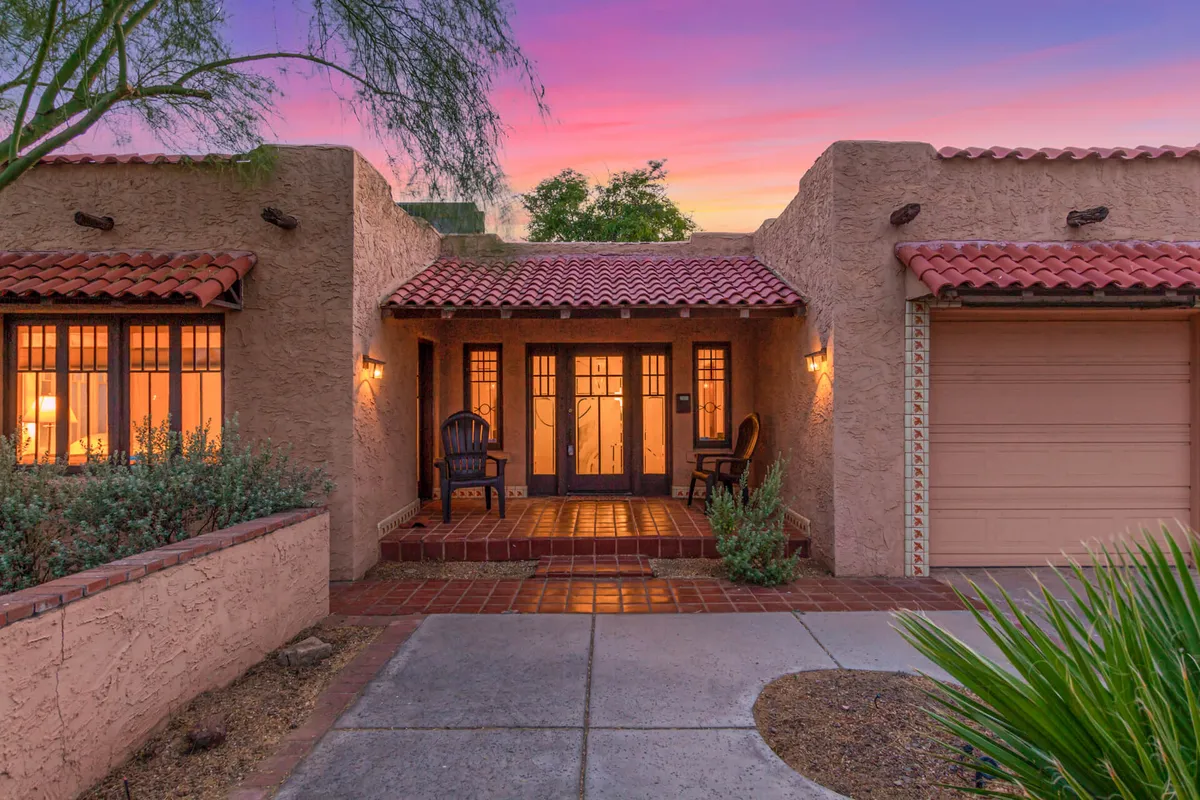 This hero image features the charming exterior of a historic single-family home in downtown Phoenix. The scene highlights a welcoming front door, cozy outdoor seating area, and a lush, landscaped garden—perfect for relaxing or socializing. Warm sunlight bathes the porch, evoking a serene and inviting mood.